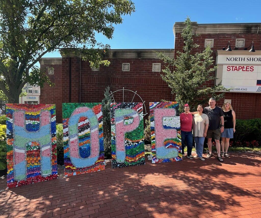 The Hope Mural is displayed outside the Staples Center in Downtown Glen Cove. Pictured are artist Amanda Fisk, Lydia Wen from Glen Cove Library, mural builder Mike Danchalski and Downtown BID Executive Director Jill Nossa.